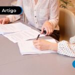 Papeis sobre uma mesa com duas pessoas escrevendo