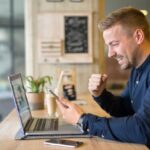 homem feliz olhando para o notebook e celular