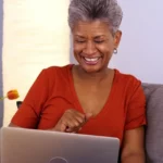 Senhora sentada no sofá sorrindo com computador no colo