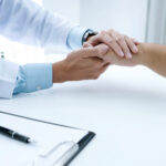 Imagem ilustra médico segurando a mão de uma paciente.