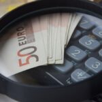 algumas notas de cinquenta sobre uma calculadora e abaixo de uma lupa.