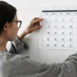 a imagem mostra uma mulher colando um calendário na parede.