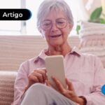 imagem de idosa sentada no sofá sorrindo enquanto mexe no celular