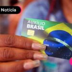 imagem de mão feminina com unhas alongadas segurando cartão do Auxílio Brasil