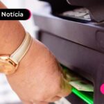 uma mão recolhendo dinheiro na boca do caixa.