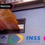 imagem de mão retirando notas de reais de boca de caixa eletônico