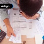 Pessoa sob uma mesa com papeis e uma calculadora
