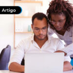 Homem sentado em uma mesa com uma mulher dando orientações a frente de um computador