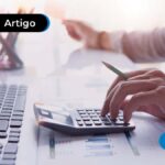Mão utilizando uma calculadora a frente de um computador
