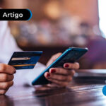Pessoa segurando um cartão em uma mão e um telefone celular na outra