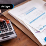 Pessoa utilizando uma calculadora sob uma pesa com papeis ao lado