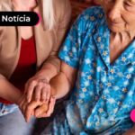 senhora de idade sentada com auxilio de outra pessoa