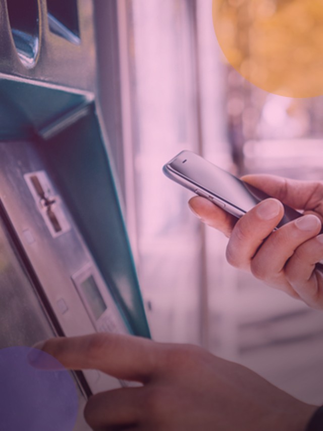Pessoa com um celular na mão a frente de um caixa eletronico