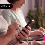 foto de mulher mexendo no celular ao lado de outra mulher mexendo no computador