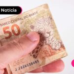 Imagem mostrando uma mão segurando nota dobrada de cinquenta reais.