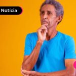 Pessoa de idade com expressão de dúvida, usando blusa azul. No fundo, uma parede laranja.
