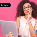 Imagem de pessoa segurando computador atrás de uma parede rosa