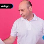 Pessoa adulta com expressão de dúvida no rosto, vestindo camiseta social branca enquanto segura papeis e tenta ler o que está escrito neles.