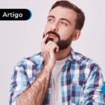 Jovem com cabelo castanho escuro e blusa quadriculada azul com a mão no queixo fazendo uma expressão de dúvida.