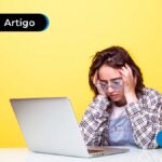 Pessoa com as mãos sobre a cabeça com expressão preocupada na frente de um computador