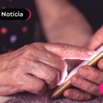 Pessoa segurando um celular e usando um dedo para tocar a tela