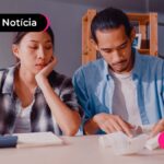 Dois jovens sentados em uma mesa de escritório com uma calculadora e várias notas espalhadas pela mesa.