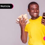 Pessoa de blusa amarela segurando notas de dinheiro e um celular