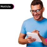 Pessoa jovem vestindo camiseta azul, sorrindo enquanto faz uma anotação em um caderno.