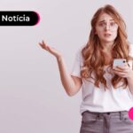 Jovem de cabelo longo vestindo roupas casuais, com expressão de dúvida no rosto enquanto segura um celular com uma das mãos.