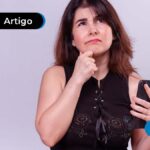 Pessoa com expressão de pensativa vestindo blusa preta e segurando um celular.