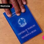 Carteira de Trabalho e Previdência Social em uma mesa com uma mão ao lado.