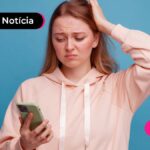 Jovem com expressão de dúvida com uma mão na cabeça e a outra segurando um celular.