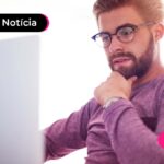 imagem de pessoa com óculos pensando ao lado de um computador