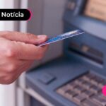 imagem de pessoa segurando cartão ao lado de um caixa eletrônico