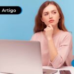 Pessoa sentada em uma mesa com um computador na sua frente