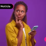 Pessoa de blusa amarela com expressão pensativa e celular em mãos