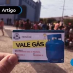Mão segurando cartão do vale-gas e ao fundo pessoas.