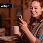 Imagem mostra pessoa jovem sorrindo enquanto lê algo no celular.