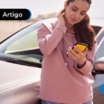 Pessoa encostada em um carro com o celular na mão