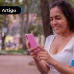 Imagem mostra jovem sorrindo mexendo no celular.