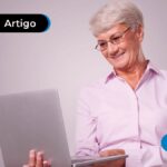 Imagem mostra pessoa de idade sorrindo olhando para tela do computador.