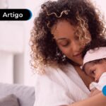 Mãe com filha bebê no colo vestindo branco e sorrindo.