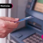Mão parda segurando cartão e se preparando para sacar dinheiro no caixa eletrônico.