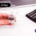 Pessoa segurando uma lampada e calculadora preta ao lado.