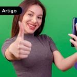 Jovem sorrindo segurando um celular e fazendo sinal de joinha com a mão.