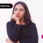 Pessoa de camisa preta com manga longa, um braço cruzado e outro levando a mão para o queixo, com expressão de chateação no rosto.