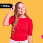 Pessoa jovem com camisa vermelha apontando com uma mão para cima e sorrindo.