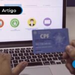 Pessoa escrevendo em um computador e segurando o cartão do CPF