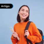 Pessoa jovem sorrindo com um moletom laranja, mochila de costas e segurando cadernos.