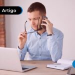 Pessoa olhando para o computador com o celular na orelha